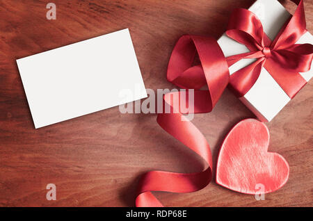 Scatola regalo bianca e nastro rosso con tag su uno sfondo di legno con lo spazio. Vintage scatola regalo su tavola di legno con spazio per il testo. Foto Stock