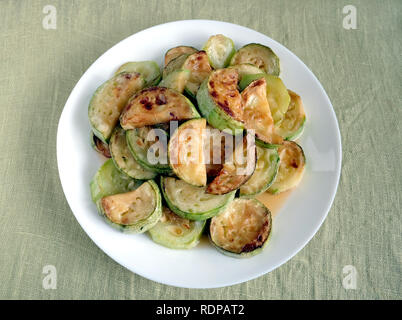 Molti fritti fette di zucchine sul round piastra bianca su tessuto verde dello sfondo vista superiore closeup Foto Stock
