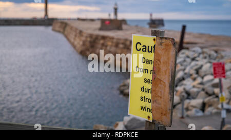 Segno: Attenzione, pericolo - mezza distrutta con la sfocata pier e il faro in background, visto a Whitby, North Yorkshire, Inghilterra, Regno Unito Foto Stock