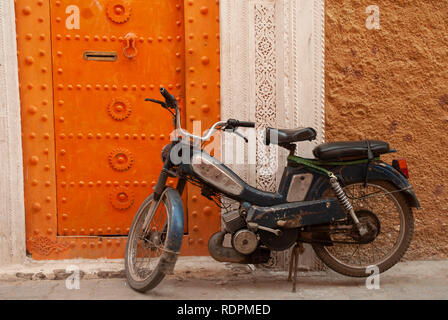 Un motociclo Parcheggiato fuori un vivacemente colorato di arancione porta, Marrakech, Marocco Foto Stock