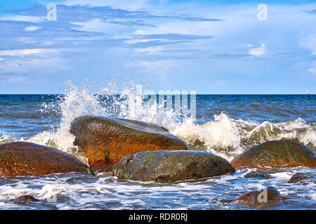 Onde bounce su grandi pietre e splash. Sullo sfondo di un bellissimo cielo con le nubi sul Mar Baltico. Foto Stock