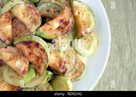 Molti fritti fette di zucchine sul round piastra bianca su tessuto verde dello sfondo vista superiore closeup Foto Stock