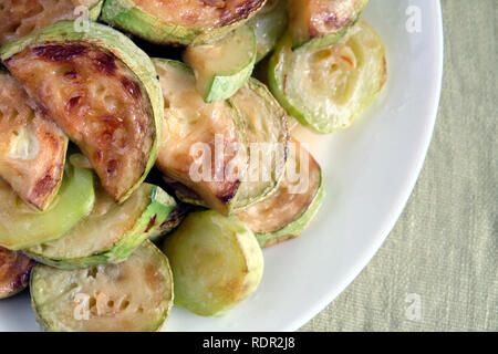 Molti fritti fette di zucchine sul round piastra bianca su tessuto verde dello sfondo vista superiore closeup Foto Stock