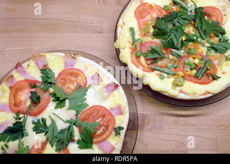 Сooked gustosa pizza fatta in casa con pomodori, pancetta, mais e piselli verdi su piastre tonde su sfondo di legno vista superiore Foto Stock