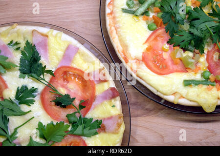 Сooked gustosa pizza fatta in casa con pomodori, pancetta, mais e piselli verdi su piastre tonde su sfondo di legno vista superiore Foto Stock