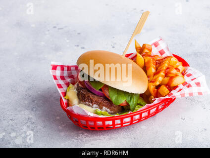 Carni bovine fresche burger con salsa di pomodoro e verdure con patatine fritte in rosso che serve cesto su pietra tavolo da cucina dello sfondo. Foto Stock