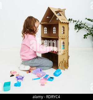 Felice bambina gioca con la casa di bambola e casa di bambola mobili. Funny bel bambino si diverte a Foto Stock