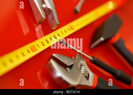 Un nastro di misurazione, un cacciavite-tap, un flex-testa chiave, e pinze giacciono su un rosso levigata in una riparazione auto shop. Strumenti meccanici. Foto Stock