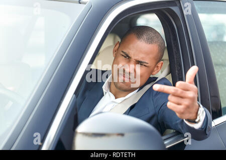 Imprenditore giovane guidatore seduto all'interno di guida auto che mostra il dito medio al di fuori offeso da un altro veicolo vista laterale di close-up Foto Stock