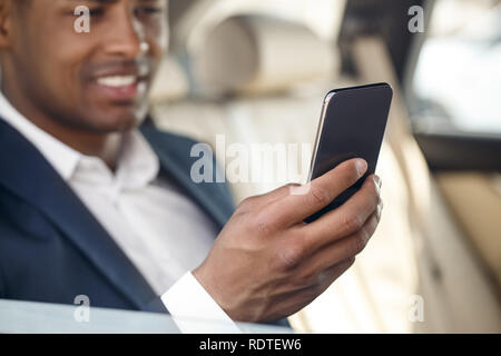 Giovane imprenditore seduto in macchina controllo supporto sullo smartphone felice close-up sfondo sfocato Foto Stock