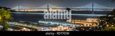 Vista panoramica della notte illuminata Bay Bridge che collega San Francisco e Oakland; terminali di traghetto e piloni in primo piano; notte foto Foto Stock