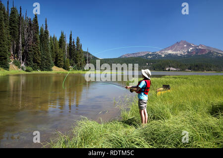 Ragazza la Pesca da riva lungo il canale al Lago di scintille, rotte Top Mountain in background, la cascata di laghi, Oregon, Stati Uniti d'America Foto Stock