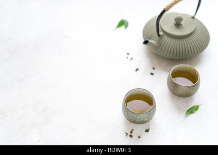 Asian Set per il tè - teiera in ferro e ceramica teacups con tè verde e foglie. Tè tradizionale composizione su sfondo bianco, copia dello spazio. Foto Stock
