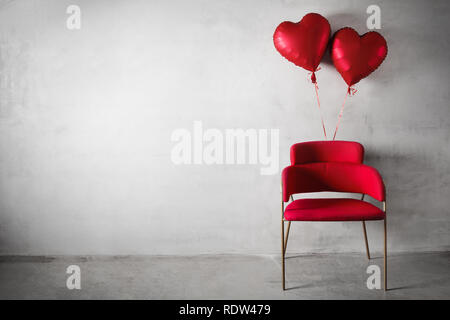 Sedia rossa con cuore di palloncini sagomati galleggiante sulla parete in calcestruzzo dello sfondo.