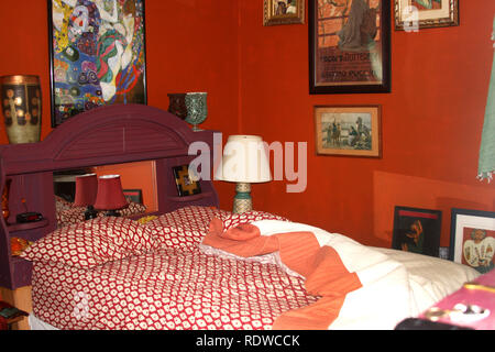 Interno della piccola camera da letto dipinta in rosso-arancione, con artwork visualizzati attorno al letto Foto Stock