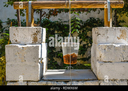 Un pozzo medievale con benna arrugginito appesi ad una fune nel giardino della chiesa di San Giovanni al Sepolcro nella città di Brindisi, Italia Foto Stock