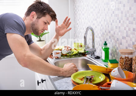 Giovane triste guardando gli utensili sporchi vicino al lavello in cucina Foto Stock