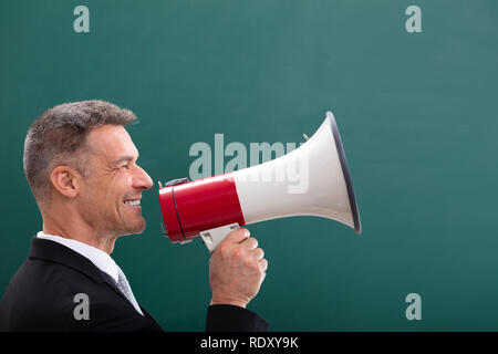 Felice uomo maturo facendo annuncio mediante megafono davanti a Lavagna Foto Stock