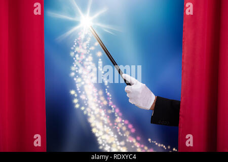Close-up del mago la mano che tiene la Bacchetta Magica rosso dietro il sipario di un palcoscenico Foto Stock