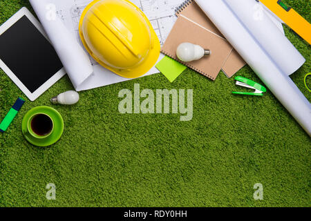 Il luogo di lavoro con casco, blueprint, laptop e blocco note su sfondo di erba. Vista da sopra con lo spazio di copia Foto Stock