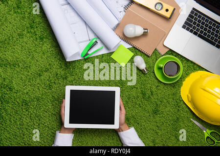 Il luogo di lavoro con casco, blueprint, laptop e blocco note su sfondo di erba. Vista da sopra con lo spazio di copia Foto Stock