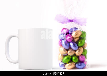 White Mug Mockup - Pasqua tema. Borsa di Pasqua mini uova di cioccolato accanto a una casella vuota white mug. Perfetto per le imprese che vendono tazze, appena sovrapporre la q Foto Stock