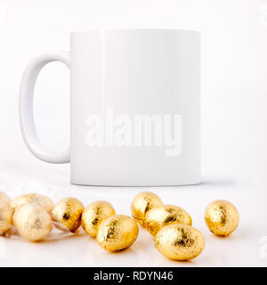 White Mug Mockup - Pasqua tema. Mini uova di pasqua di cioccolato proprio di fronte a una schermata bianca vuota mug. Perfetto per le imprese che vendono tazze, appena sovrapporre il tuo preventivo Foto Stock