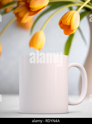 White Mug Mockup - Pasqua tema. Vuoto tazza bianca accanto al grazioso tulipani arancione. Perfetto per le imprese che vendono tazze, sovrapposizione appena il vostro preventivo o di progettazione Foto Stock