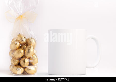 White Mug Mockup - Pasqua tema. Borsa di Pasqua mini uova di cioccolato accanto a una casella vuota white mug. Perfetto per le imprese che vendono tazze, appena sovrapporre la q Foto Stock