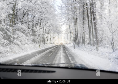 Vista attraverso il parabrezza durante la guida pericolosamente su una brutta strada forestale nella neve, copia dello spazio, messa a fuoco selezionata Foto Stock