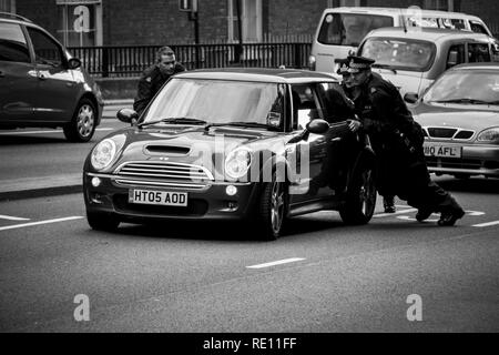 Tre inglesi ufficiali della polizia in uniforme spingendo una Mini Cooper dopo una rottura dalla corsia di destra in direzione di un più adeguato sistema di spot - Londra, Regno Unito Foto Stock