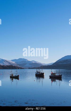 Barche da pesca riflessioni ormeggiata in Loch Ginestra, Ullapool, con nevoso inverno montagne sullo sfondo Foto Stock