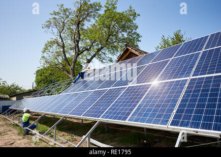 Due tecnici che lavorano sulla parte esterna del pannello solare foto voltaiche di installazione del sistema su piattaforma in acciaio su soleggiate giornate estive sotto il cielo blu. Fonti ecologiche di energia verde il concetto di produzione. Foto Stock