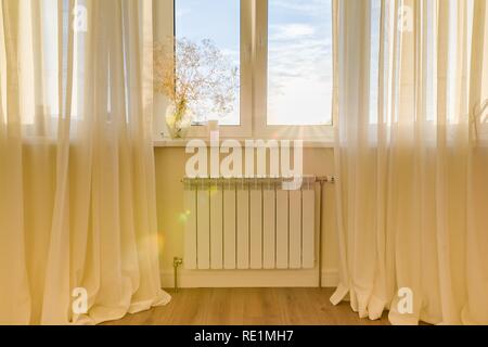 Radiatore bianco con termostato nell'appartamento. Riscaldante sotto la finestra Foto Stock