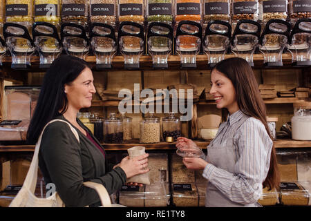 Sorridente shop assistant e permanente del cliente nei confronti di ogni altro nel pacchetto gratuito drogheria. Rifiuti Zero shopping - negoziante di servire il cliente. Foto Stock