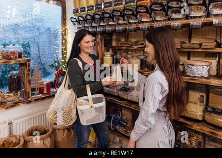 Rifiuti Zero shopping - donna acquistare cibo sano nel pacchetto free store. Allegro negoziante aiutando il cliente nel confezionamento free shop. Foto Stock