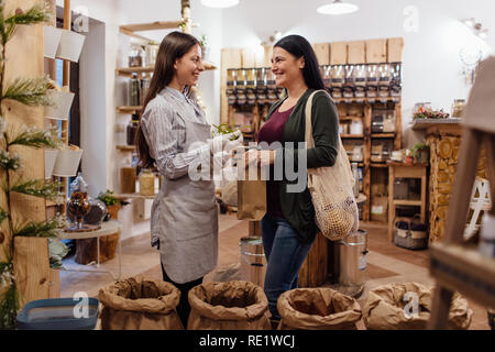 Sorridente al negoziante aiutando il cliente nel confezionamento free shop. Rifiuti Zero shopping - donna comprare prodotti freschi a pacchetto gratuito drogheria. Foto Stock