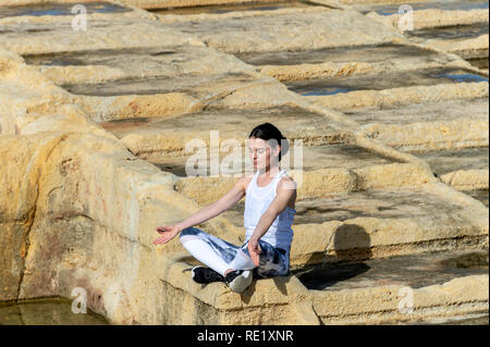 Donna meditando, seduto tra calcare le saline di Malta Foto Stock