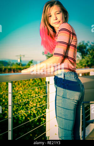 Tween ragazza alla moda capelli rosa, indossano jeans, sorride leggermente mentre lei stessa di controventamento sulla ringhiera di balcone esterno Foto Stock