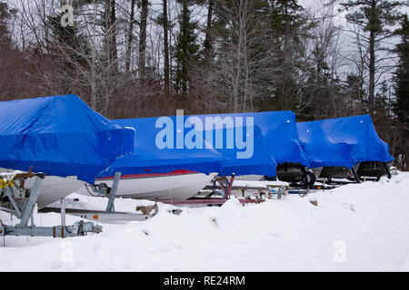 Una fila di barche seduti sui rimorchi nella coperta di neve con polimero blu film plastico termoretraibile per protezione in speculatore, NY USA Foto Stock