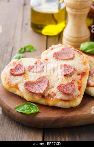 Cotto al forno a forma di cuore salsiccia per pizza fatta in casa mini pizza su una tavola di legno che serve board. Cena romantica concetto. Foto Stock