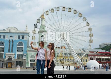 Città europea, intrattenimento ruota panoramica sulla piazza. Le ragazze giovani turisti vengono fotografati in background di Ferris wh Foto Stock