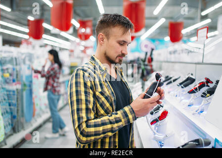 L'uomo con la rasatura elettrica macchina, matura in un supermercato. Maschio e femmina i clienti sulla famiglia shopping. L uomo e la donna l'acquisto di beni per la casa Foto Stock