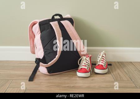 Scuola zaino e sneakers sul pavimento in un interno di casa Foto Stock