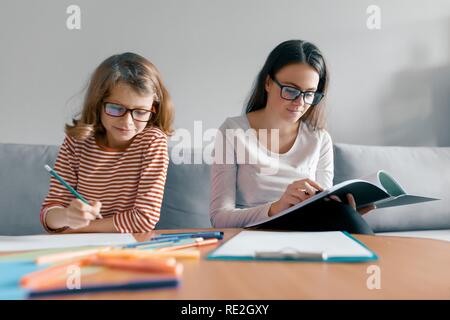 Giovane insegnante femminile dando lezione privata per bambino e bambina seduto alla sua scrivania iscritto nel notebook. Foto Stock