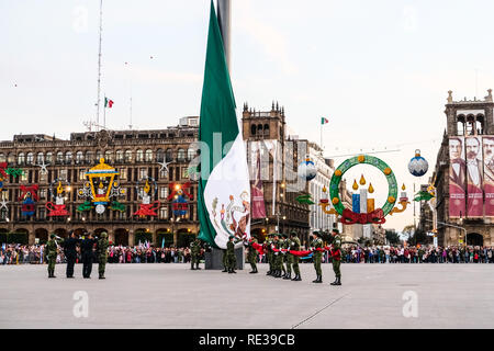 La polizia militare cadre tenendo giù il Messico bandiera nazionale al Zocalo, Città del Messico, con la gente a guardare Foto Stock