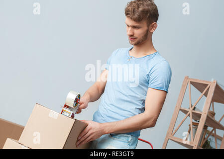 Giovane uomo che si muove di nuovo posto in piedi tenendo un nastro Scotch scatola di imballaggio a sorridere pensando Foto Stock