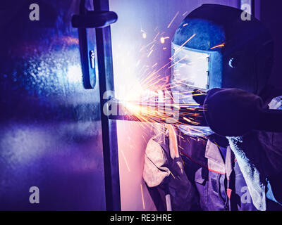 Saldatore lavoratore esegue la saldatura di salto. Lavoratore saldatore Arc-Welding esegue il processo di strutture metalliche. Scintille volanti dalla macchina di saldatura. Saldature saldatore profili metallici per il secondo piano in ambienti interni Foto Stock