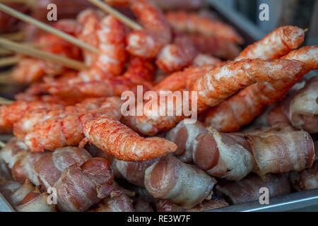 Una vasta selezione di cibi cotti cibo di strada pronti per la selezione e la vendita. I suini nelle coperte e carne di pesce su bastoni. Foto Stock