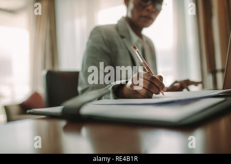 Imprenditrice seduta alla camera di albergo desk scrivendo sul documento. Focus sulla mano femmina rendendo note mentre si lavora in camera hotel scrivania. Foto Stock